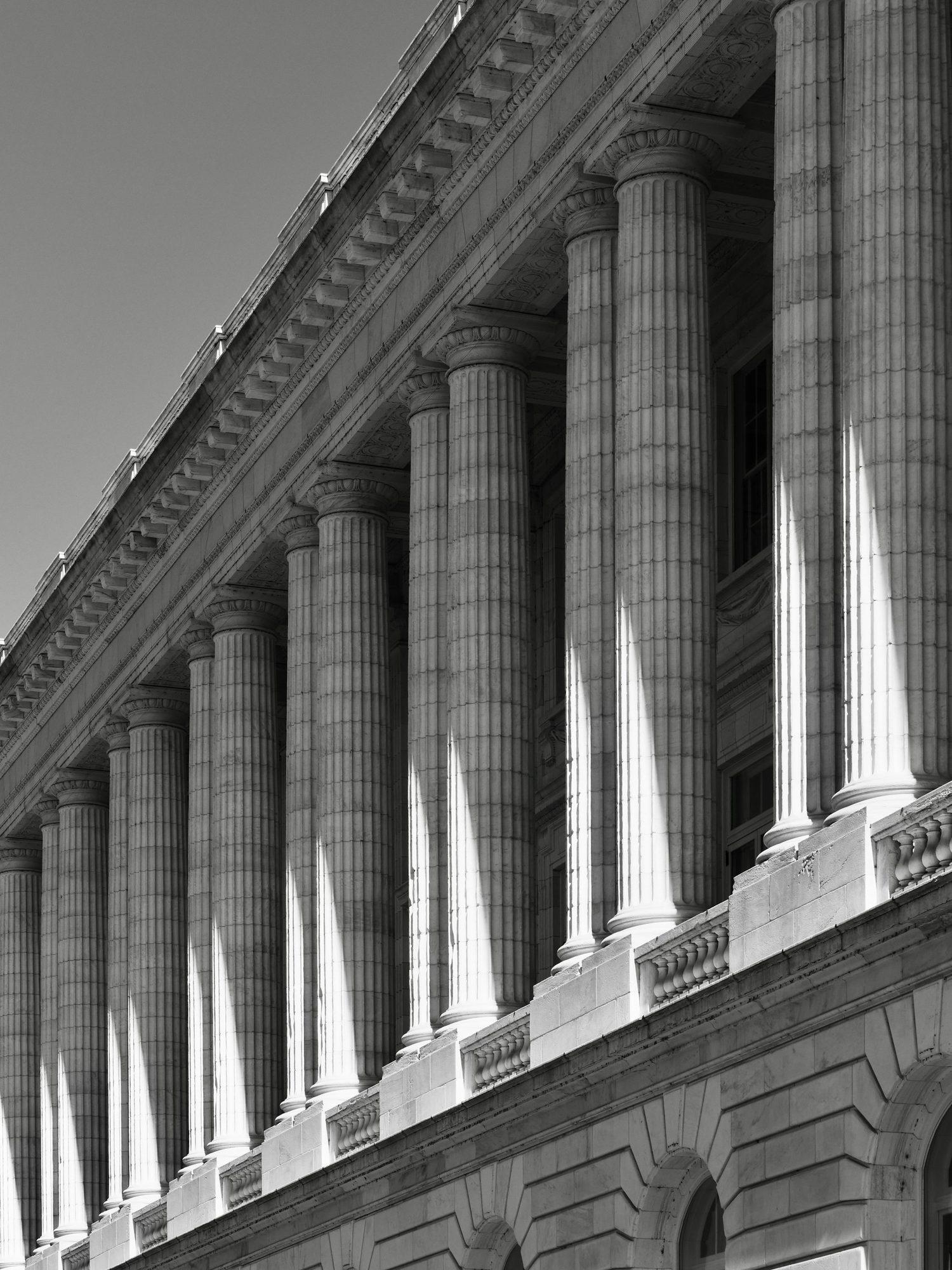 Looking up at a row of fluted stone columns on a classical building, in strong sunlight and shadow.