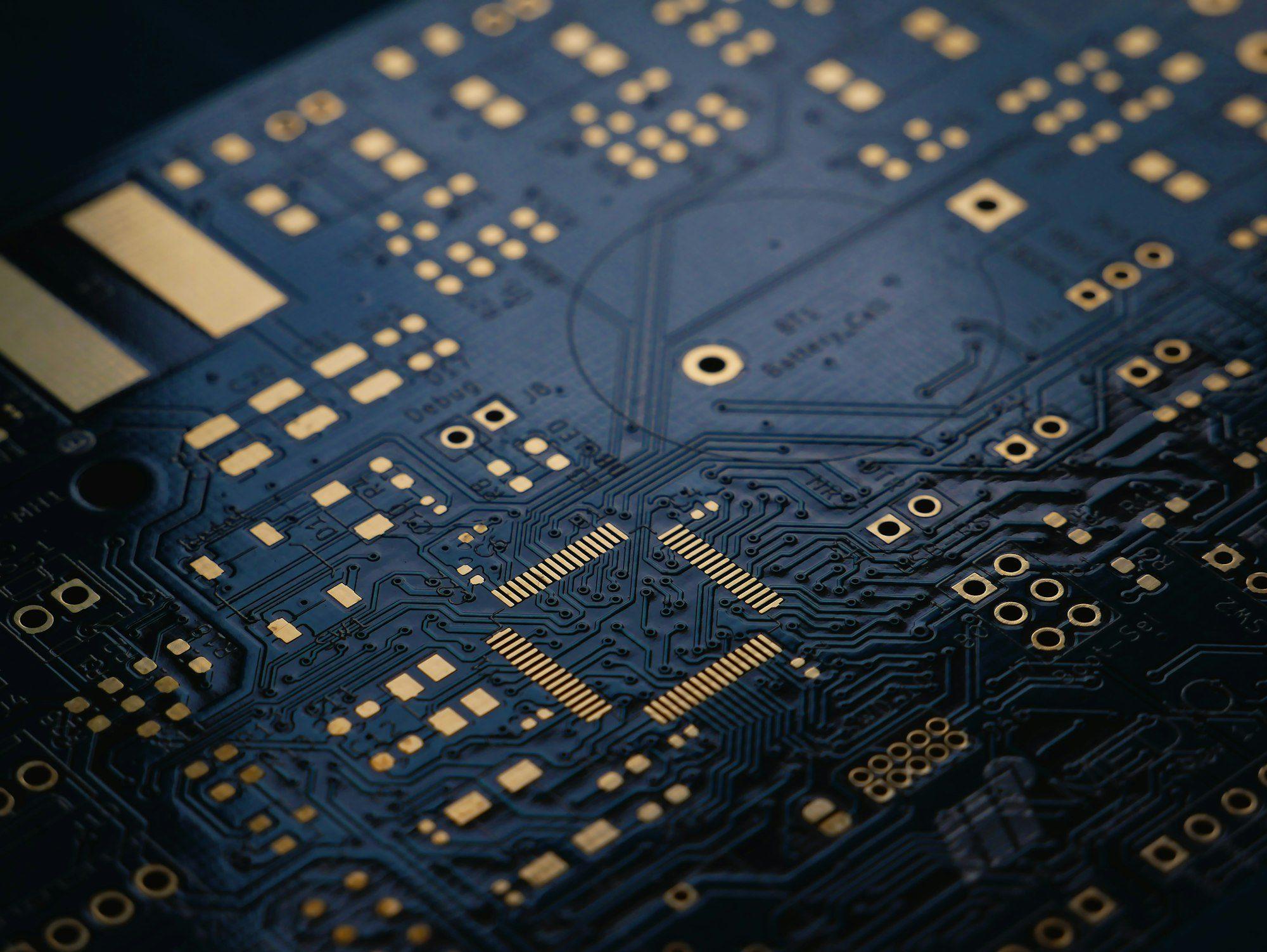Macro photograph of a dark circuit board with gold contact pads and fine traces.