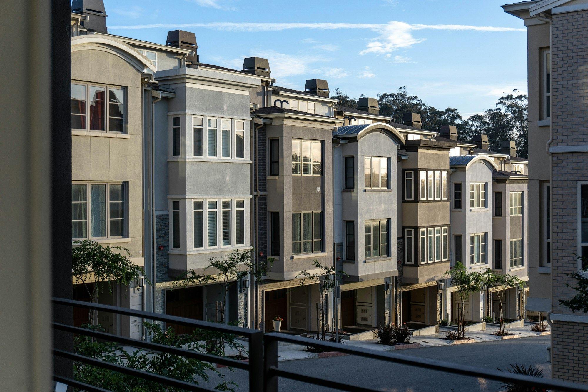 A row of modern three-storey townhouses with bay windows and young street trees on a sunny day.