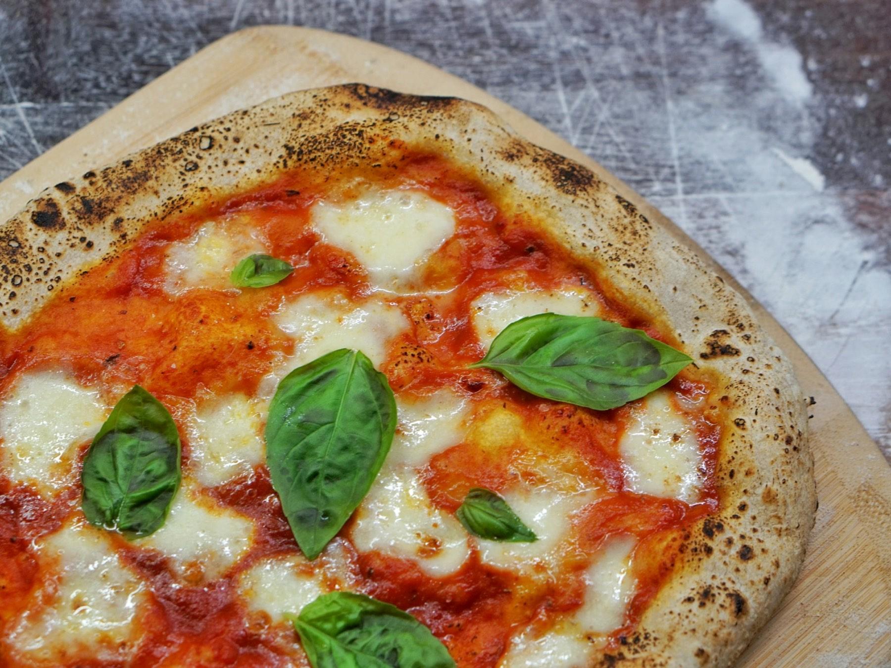 Close-up of a margherita pizza with a charred, blistered crust, mozzarella and basil on a wooden peel.