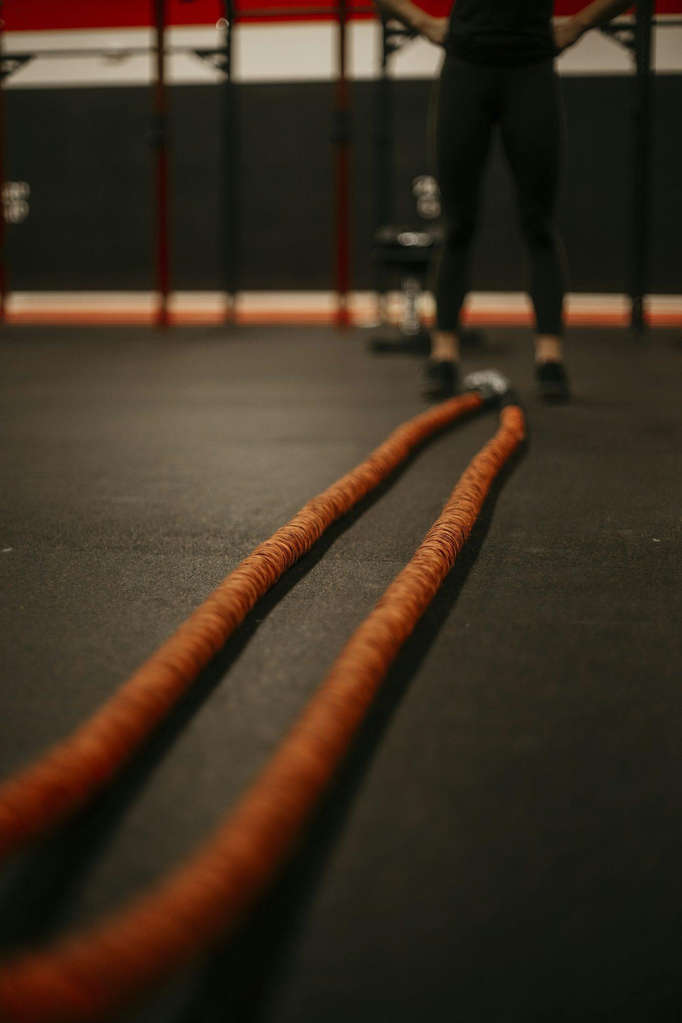 Two battle ropes stretched across a dark gym floor toward an athlete.